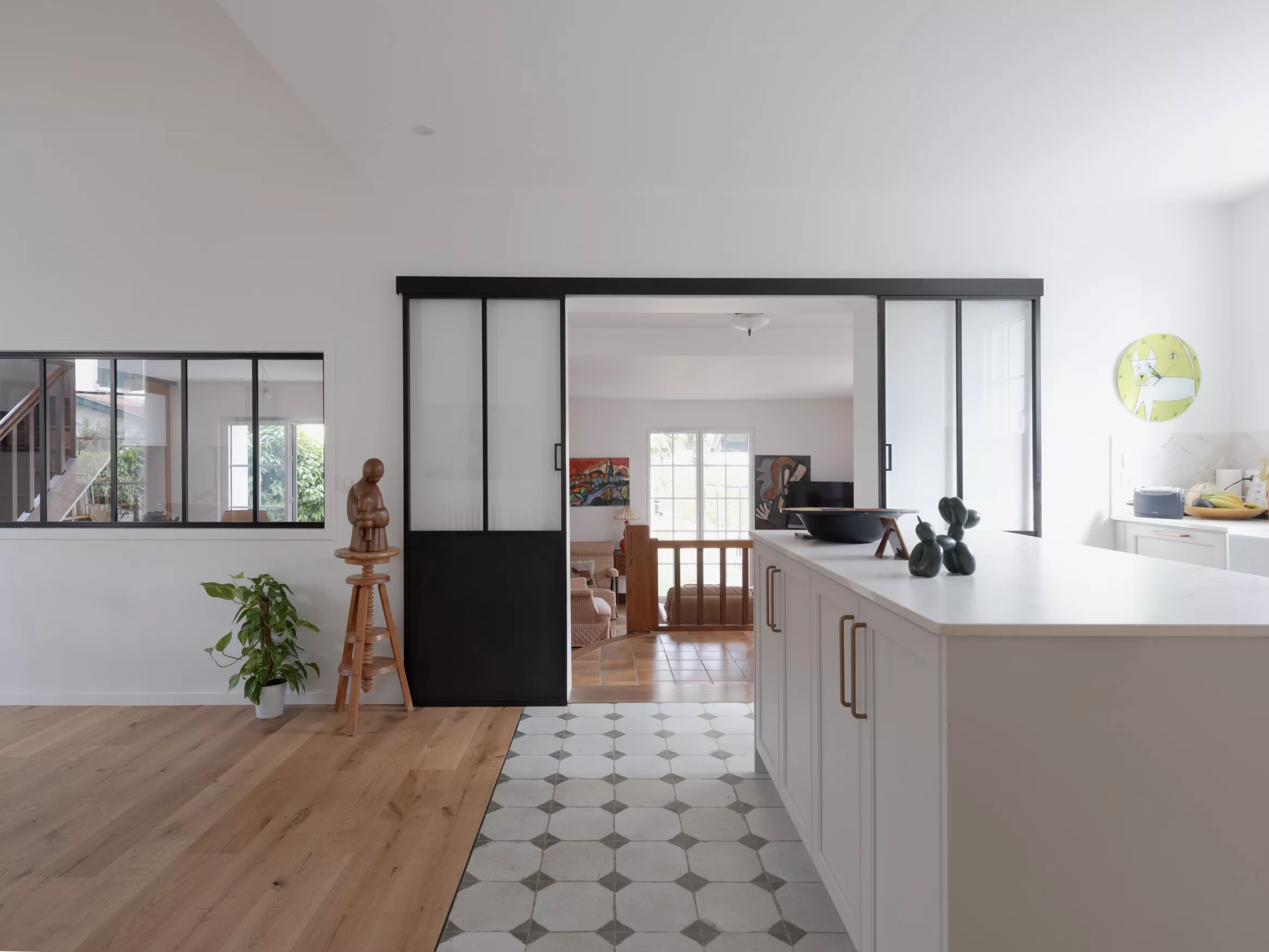 Cuisine ouverte sur la salle à manger par une verrière coulissante en acier noir, carreaux de ciment et parquet chêne