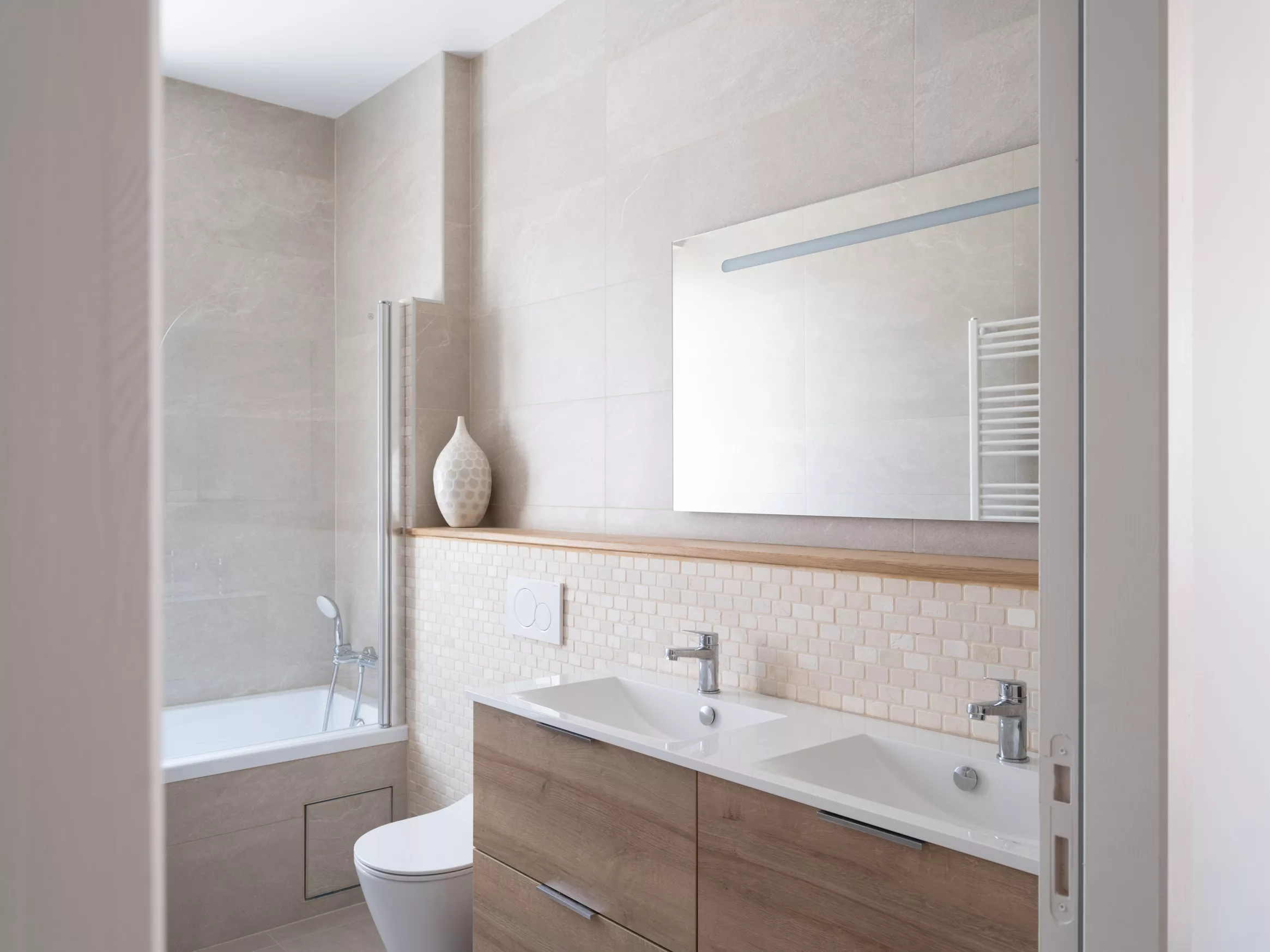 Salle de bains avec baignoire, double vasque sur meuble bois et mosaïque de pierre, éclairée par une fenêtre